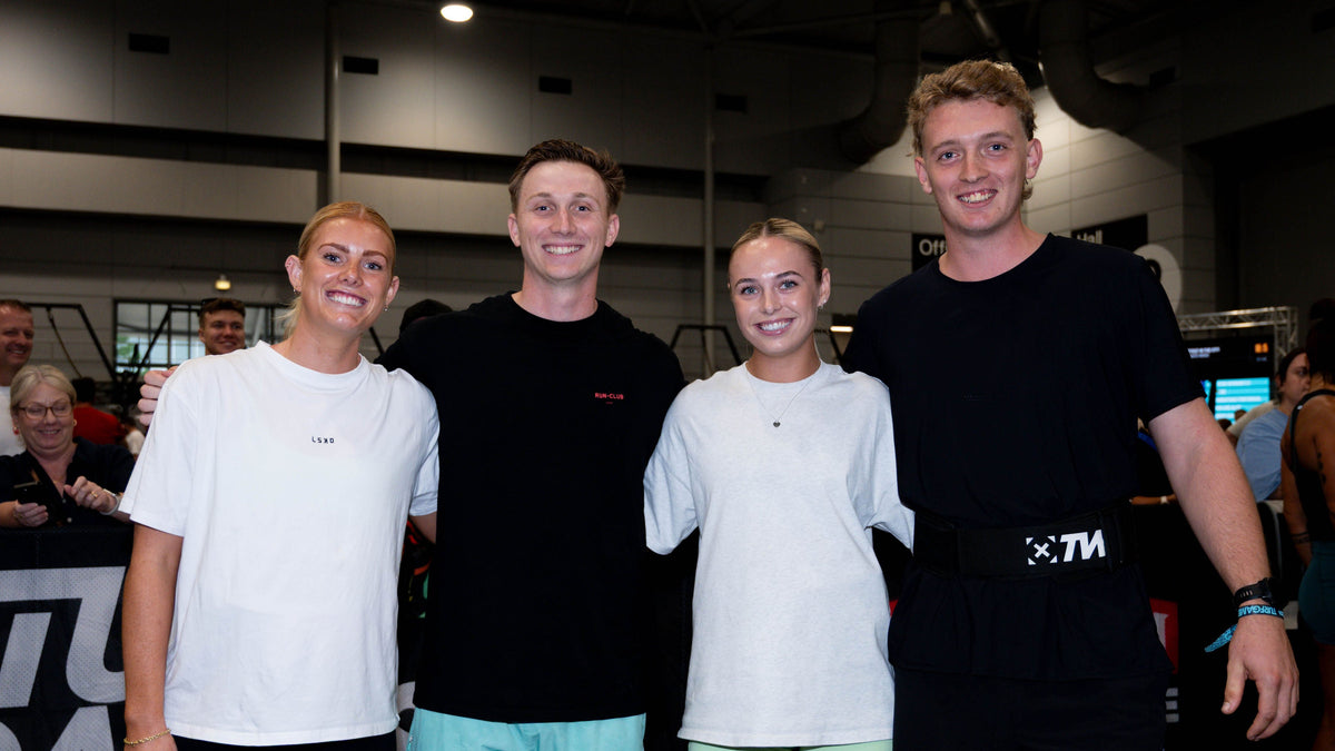 Four athletes posing together in a gym setting, wearing athletic apparel including white and black t-shirts and shorts.